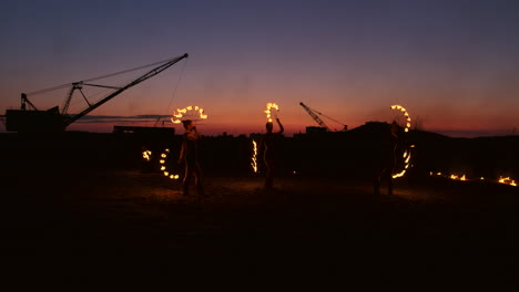 Professional-artists-show-a-fire-show-at-a-summer-festival-on-the-sand-in-slow-motion.-Fourth-person-acrobats-from-circus-work-with-fire-at-night-on-the-beach